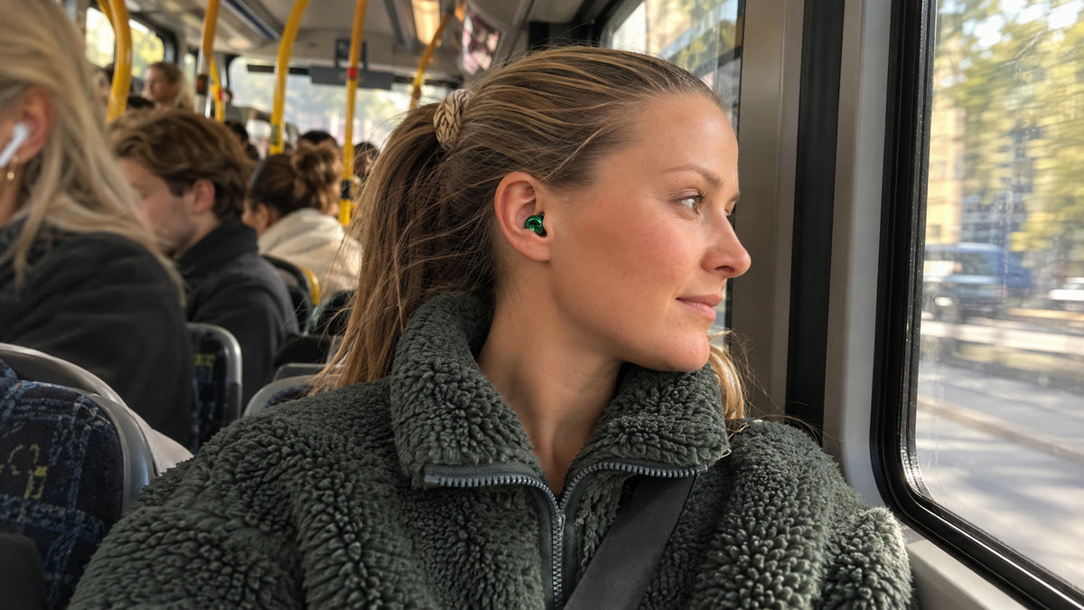 Kvinna sitter lugnt vid fönstret på en fullsatt buss med The Beat One i grönt i örat